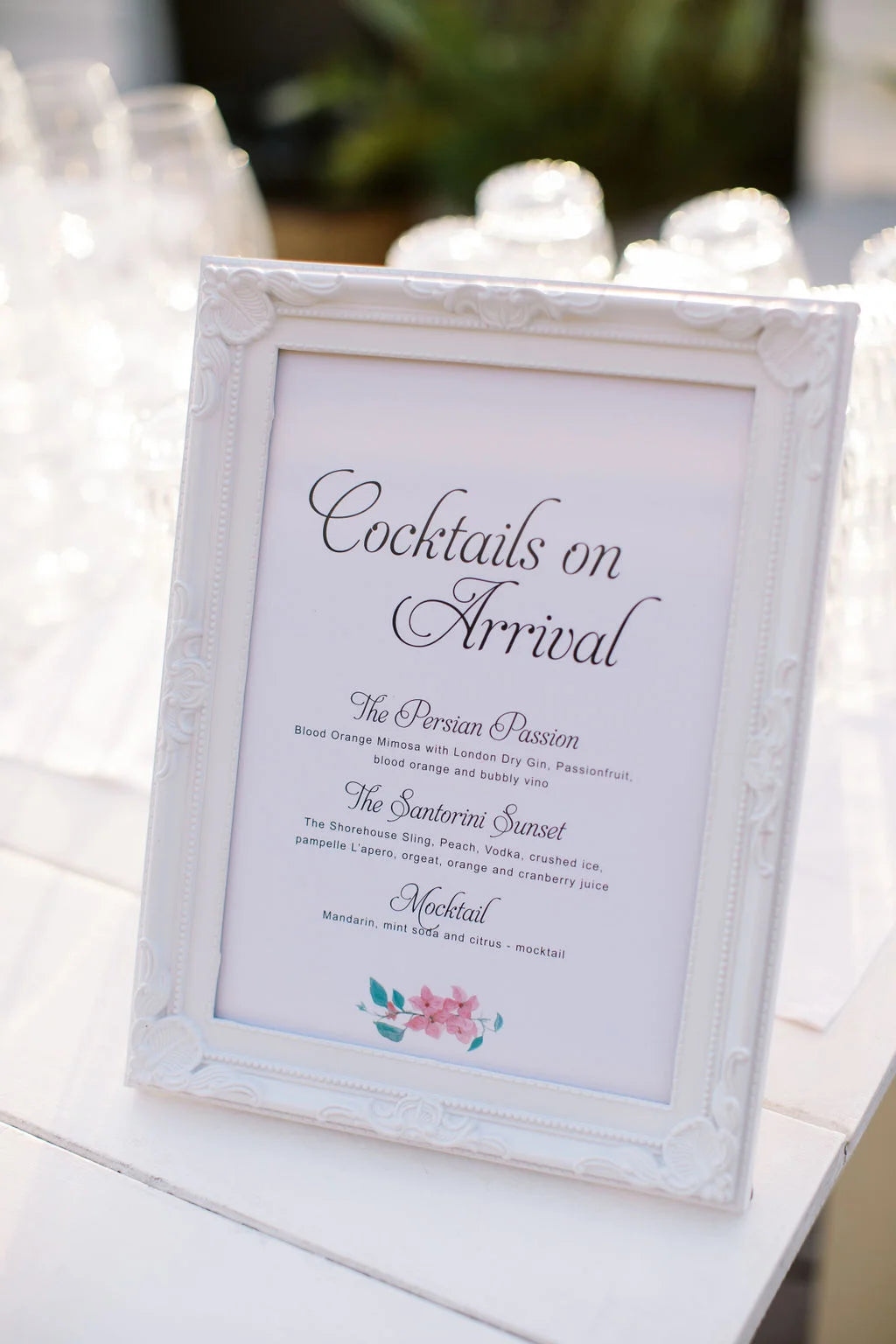 Classic framed cocktail menu sign with elegant black script, adorned with a small floral illustration.