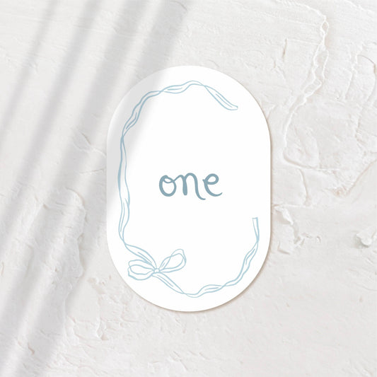 Oval table number card with “One” in script, surrounded by soft shadows.