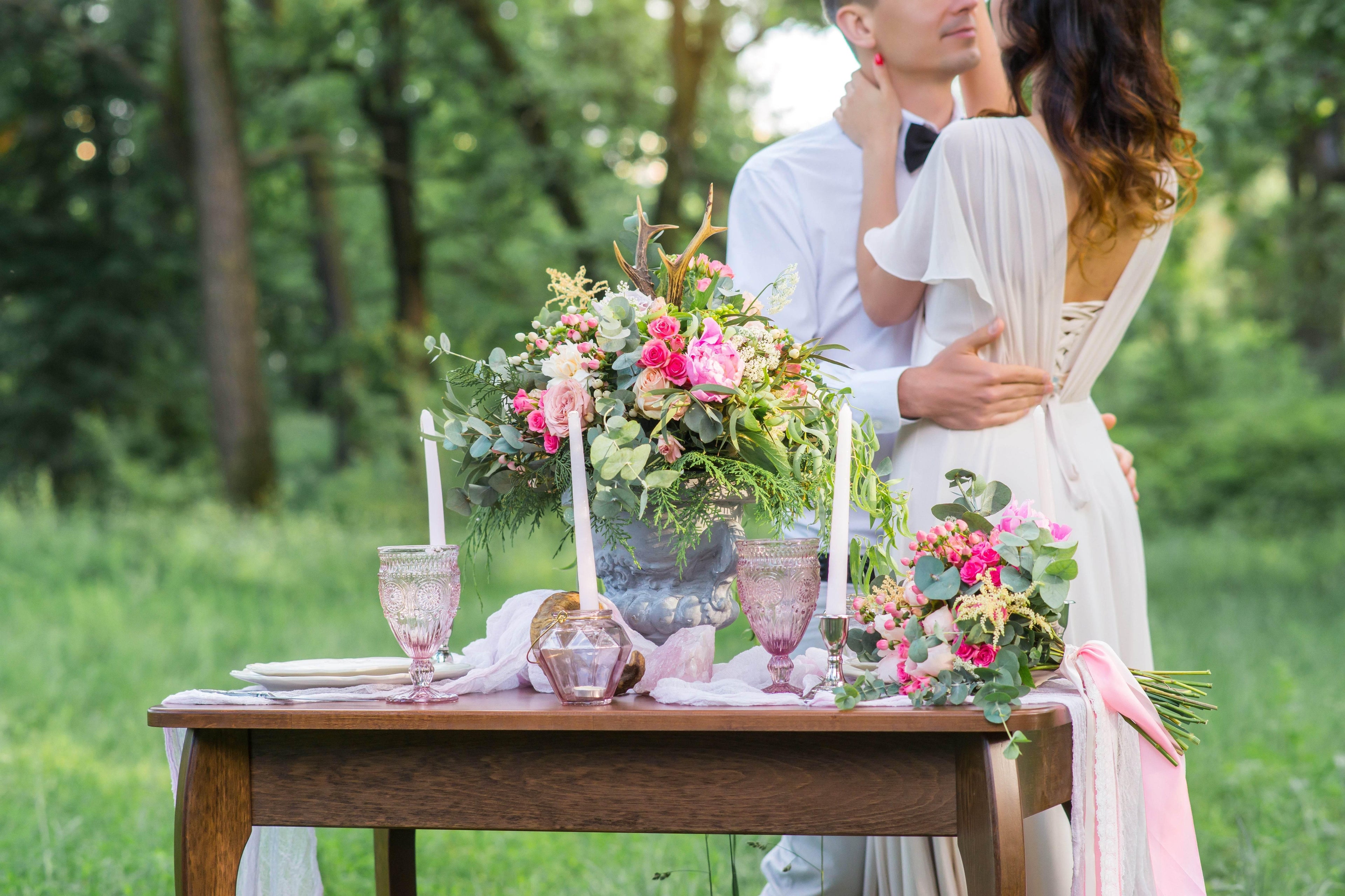 Romantic outdoor wedding setup with floral decor and embracing couple in the background.