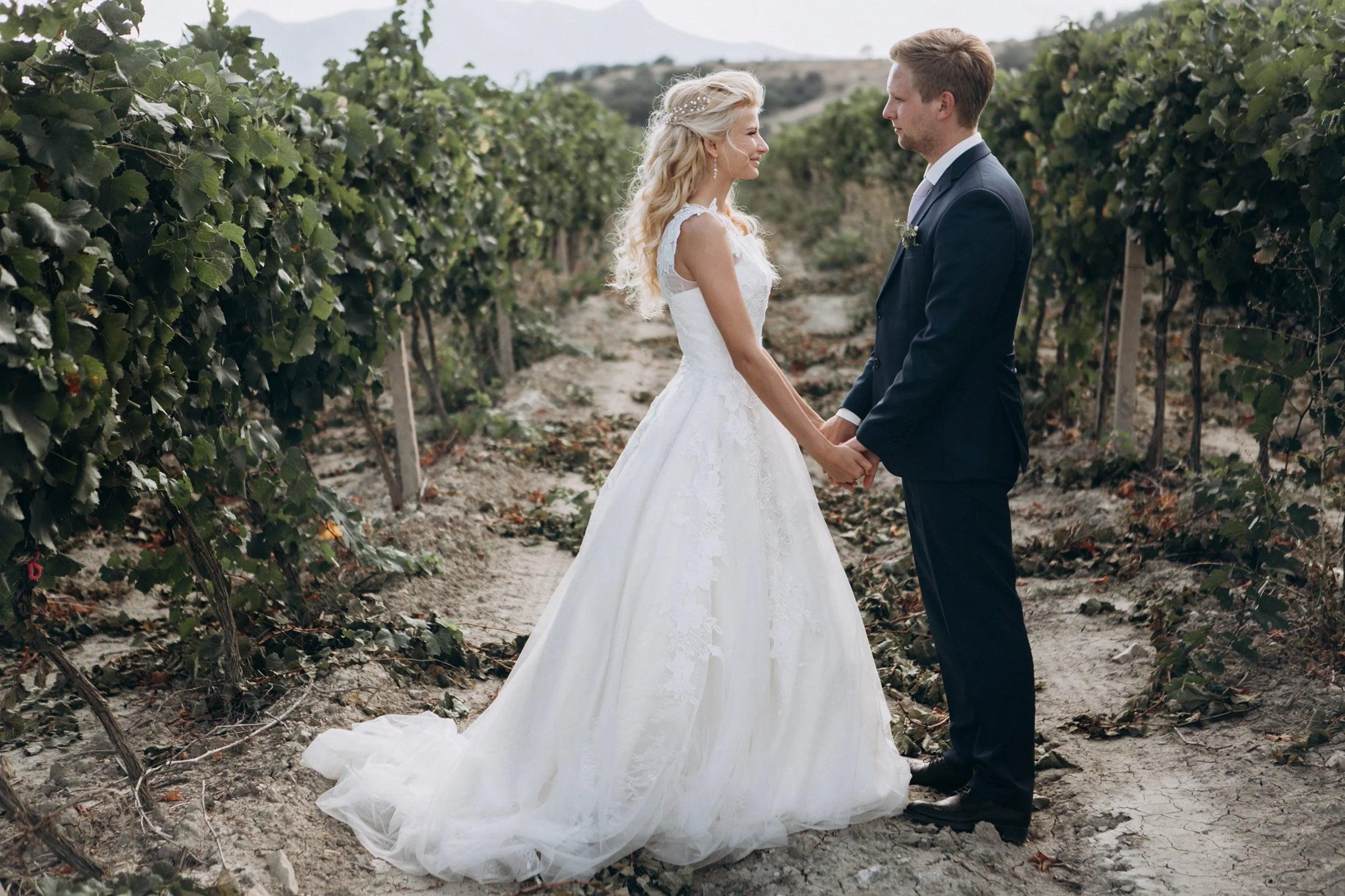 Bride and groom holding hands in a romantic vineyard setting on their wedding day.