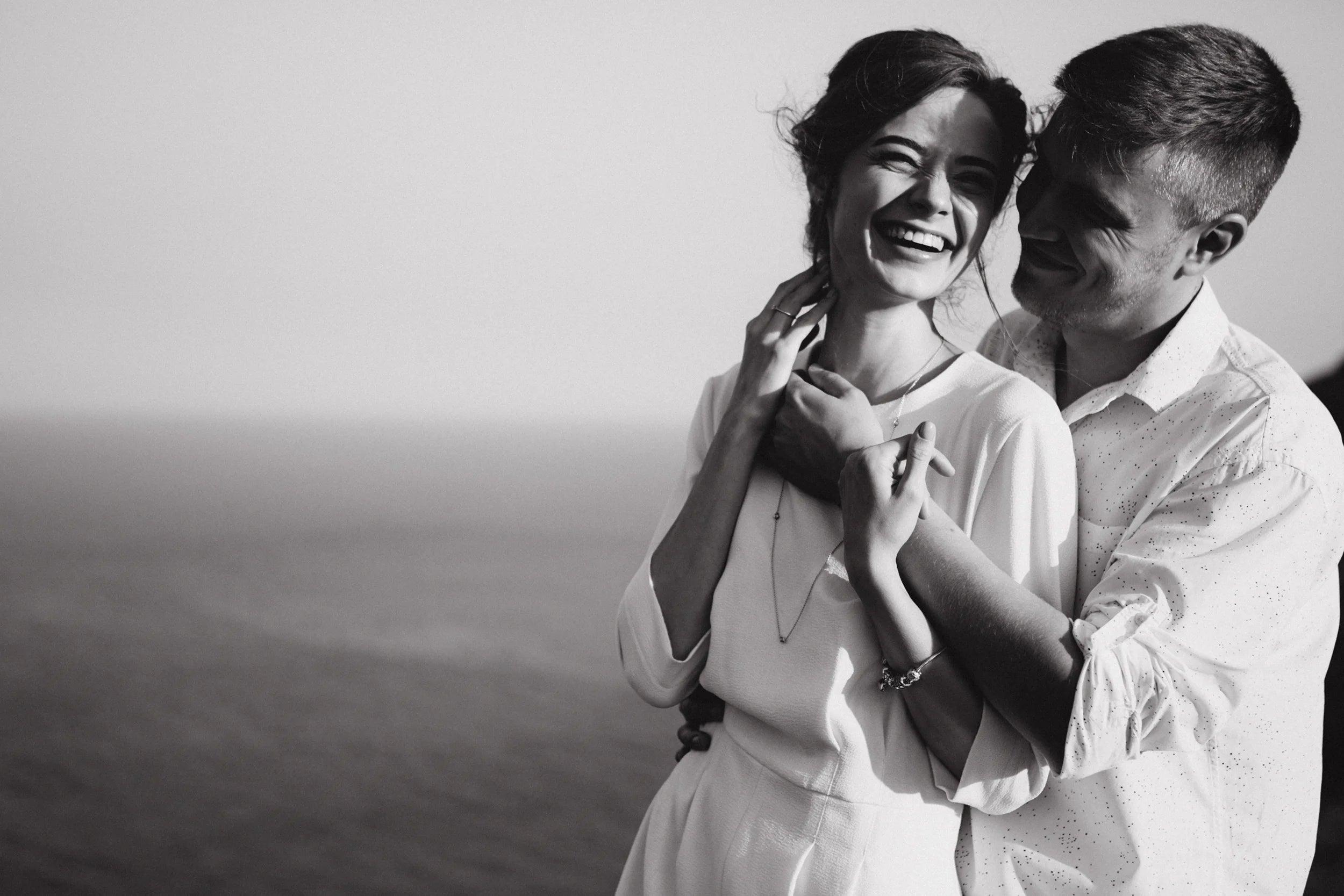 Black and white photo of a joyful couple embracing by the ocean, sharing a happy wedding moment
