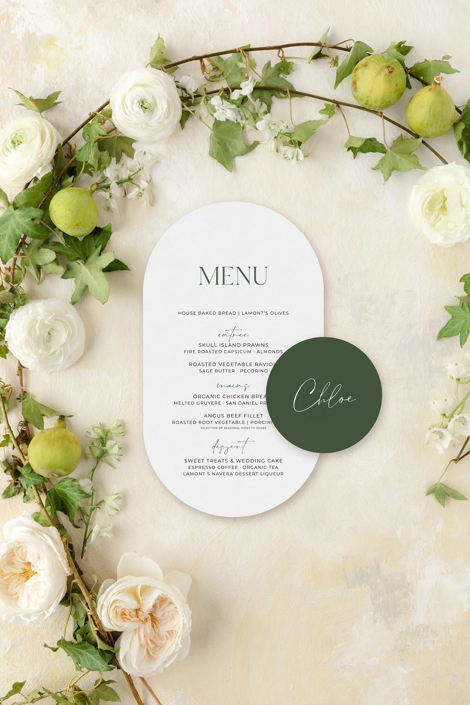 White oval wedding menu with a matching green place card reading "Chloe," styled alongside green and white floral accents.